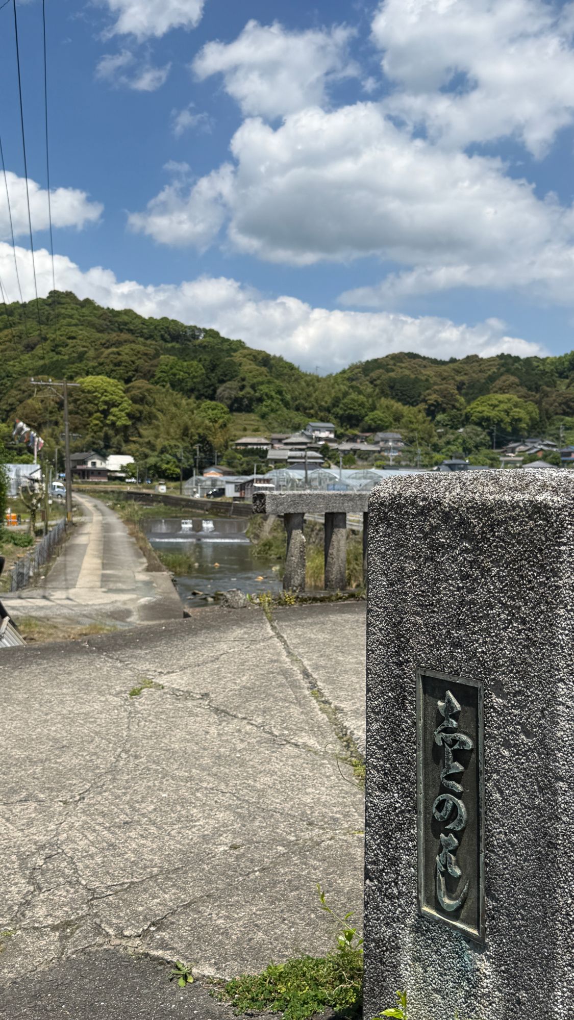 「しとのはし」ときざまれた石の親柱。そのむこうに石の橋と川、家なみと緑の山が見える